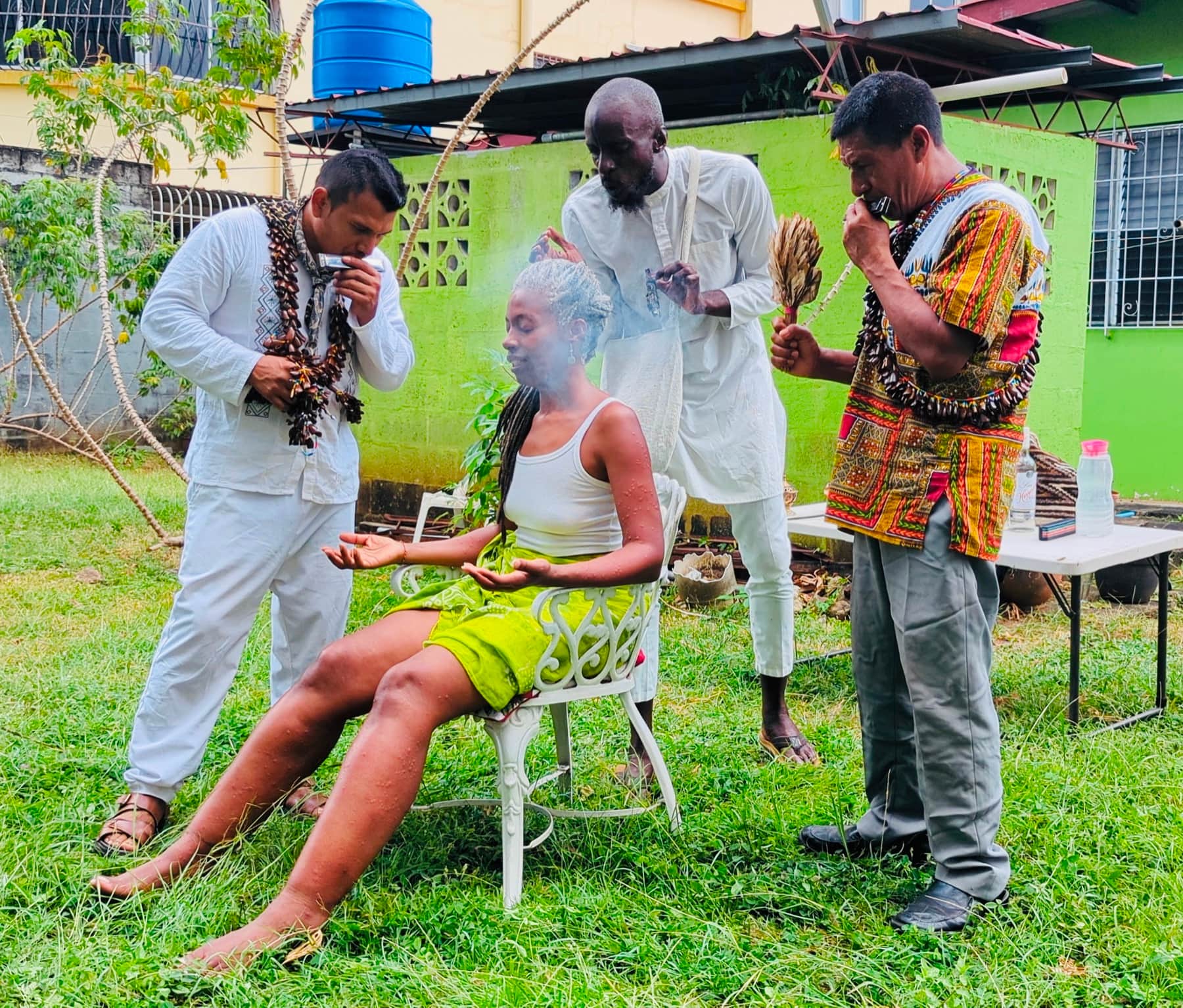 A participant seated outdoors while three ceremonial practitioners stand around them