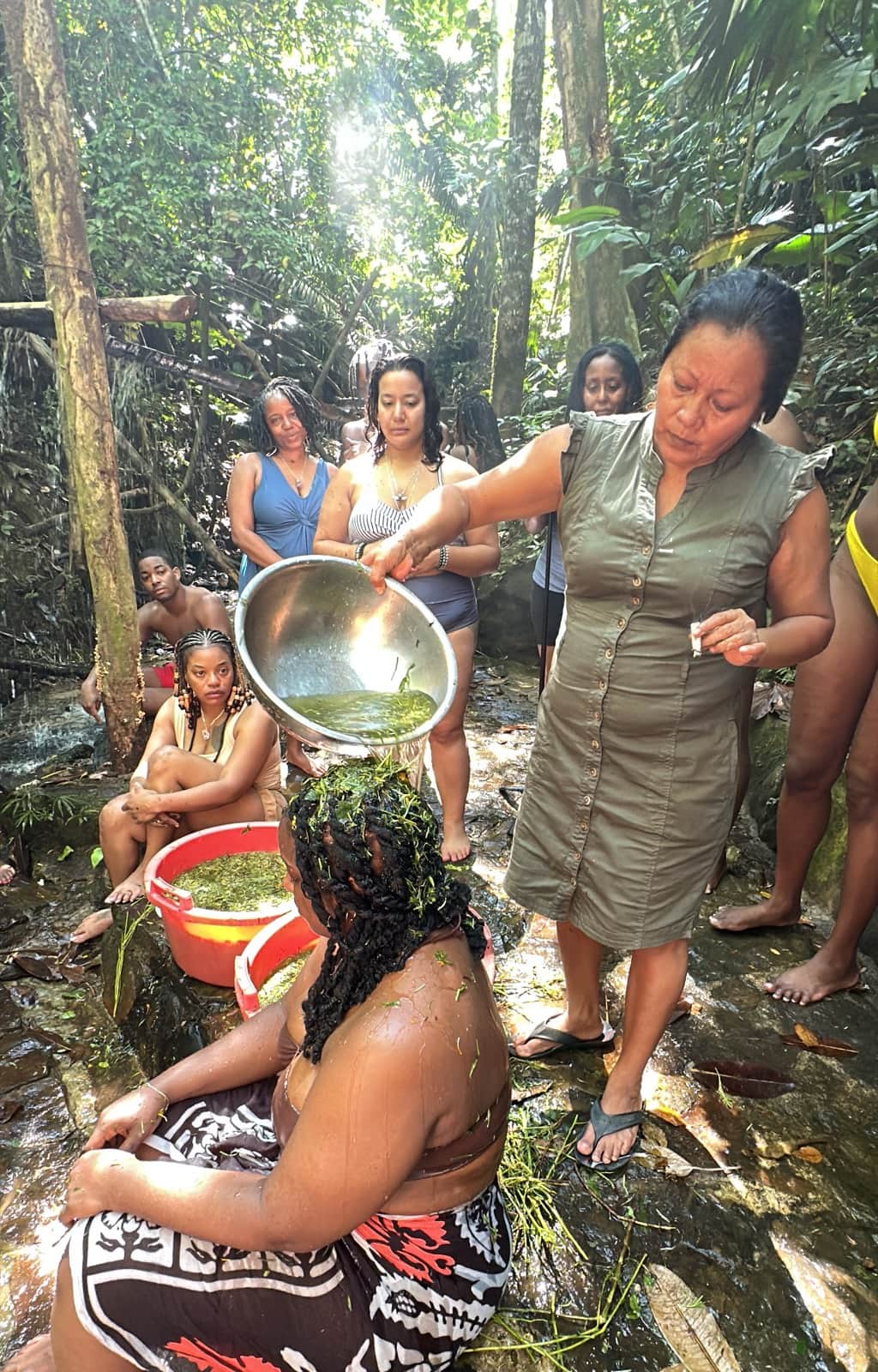 An Indigenous teacher pouring a plant preparation over a participant during a forest learning activity