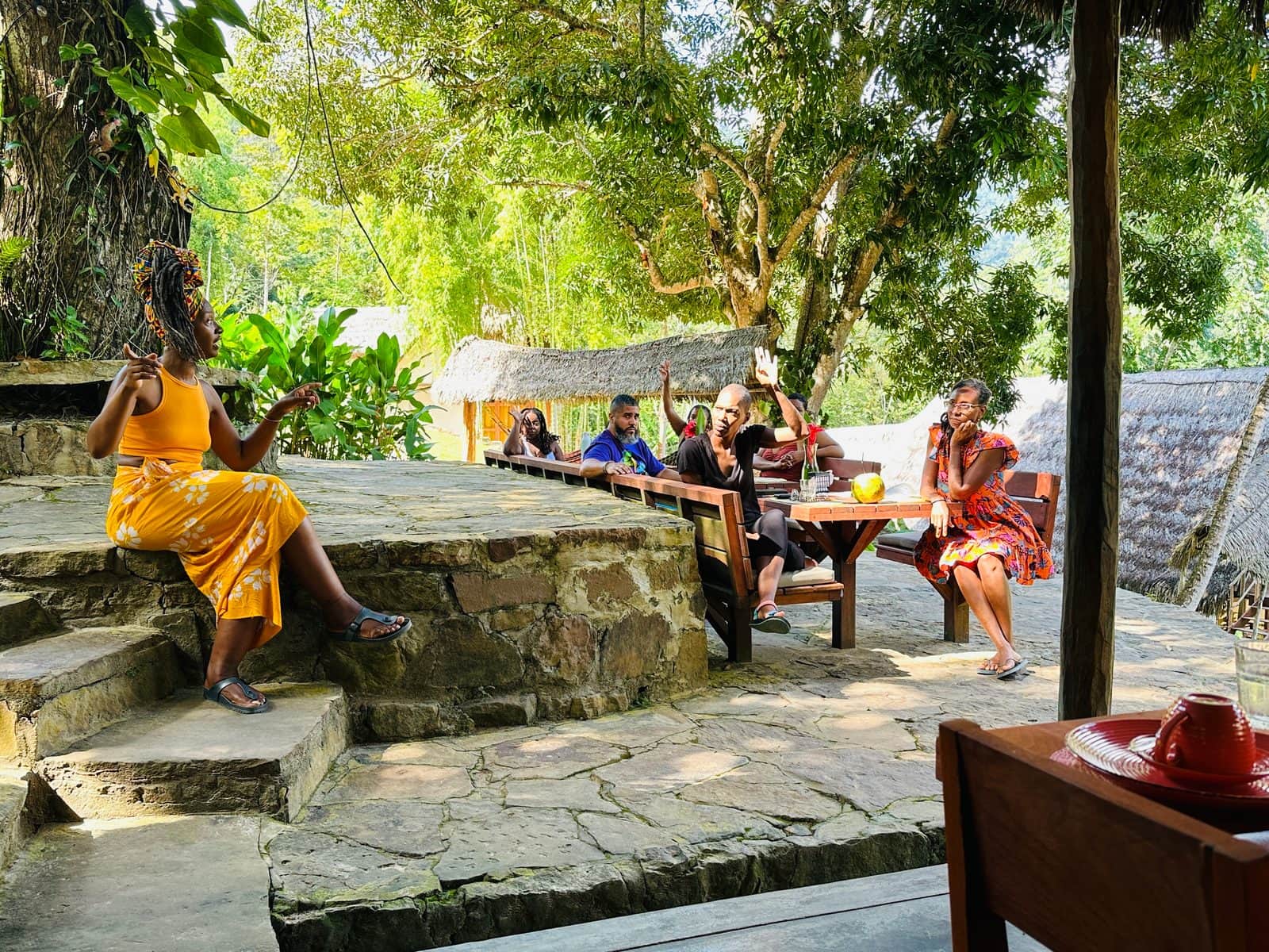 Althea speaking with a seated group at an outdoor table under trees